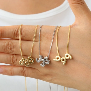 Gros plan des colliers chiffres d'ange 888 333 999 en or 18 carats et argent tenus à la main