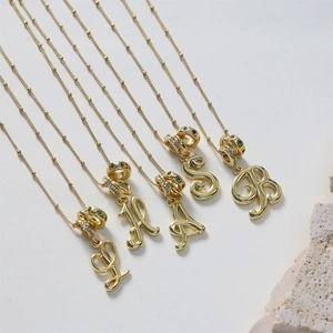 Dettaglio di ciondoli con lettere corsive in oro 18k con zirconi verdi e bianchi incastonati