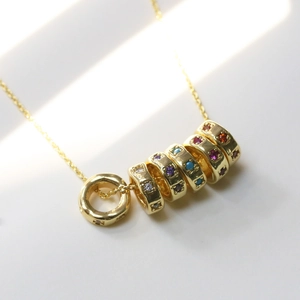 Golden necklace with six circular pendants featuring multicolor zircon birthstones on white surface