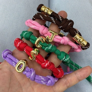Détail de bracelets en corde tressée avec breloques lettres dorées et fermoirs magnétiques