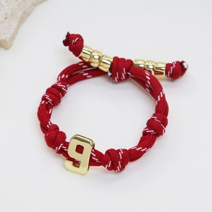 Detail of red braided lucky number 9 bracelet with gold beads and athletic cord style