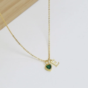 Dettaglio della collana dorata con pietra portafortuna a cuore verde e lettera E