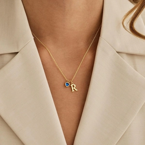 Dettaglio della collana d'oro con pietra portafortuna a cuore blu e ciondolo lettera R