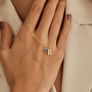 Dettaglio di collana dorata personalizzata con pietra blu a cuore e lettera R su modella