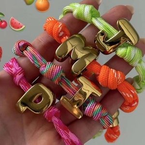 Detail von bunten geflochtenen Armbändern mit großen goldenen 3D-Alphabet-Anhängern