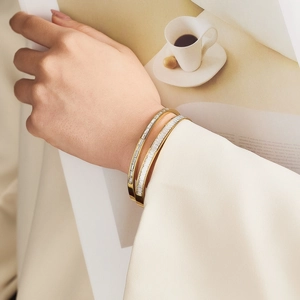 Detalle de brazalete de acero inoxidable dorado con circonitas cuadradas en la muñeca
