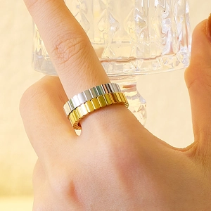 Detalle de anillos apilables dorados y plateados con ranuras verticales en el dedo de una modelo
