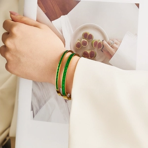 Detalle de brazaletes de acero inoxidable dorado con piedras rectangulares de color verde esmeralda