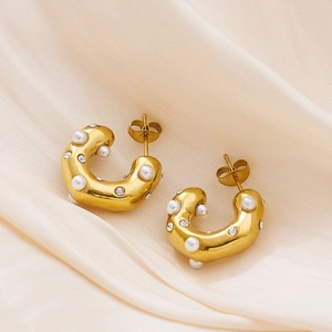 Detail of 18k gold plated chunky C-shaped earrings with pearls and crystals on silk