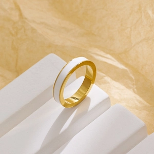 Dettaglio anello in acciaio inossidabile dorato con smalto bianco su supporto geometrico