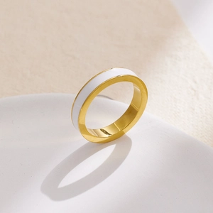 Vista macro di un anello in acciaio dorato con elegante inserto in smalto bianco lucido