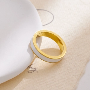 Dettaglio ravvicinato di un anello largo placcato oro con smalto bianco su carta ruvida