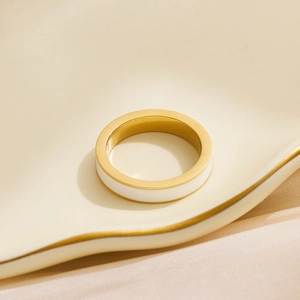 Dettaglio di un anello minimalista in acciaio dorato con inserto in smalto bianco su vassoio