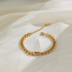 Detail of gold Cuban chain bracelet featuring a pink rectangular zircon on white silk