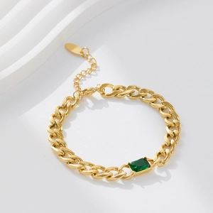 Macro view of gold Cuban chain bracelet featuring a green emerald-cut zircon stone