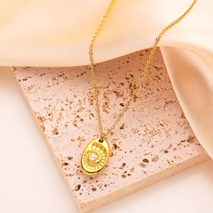 Gros plan du pendentif ovale doré avec perle sur un fond en travertin beige