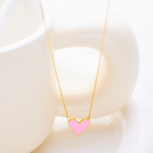 Detail of pink enamel heart pendant on gold chain draped over a white ceramic cup
