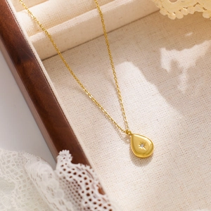 Détail d'un pendentif goutte d'eau dorée avec gravure d'étoile et zircon dans une boîte