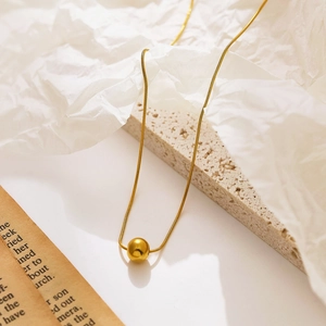 Gros plan sur collier chaîne serpent dorée avec pendentif perle sur support en pierre