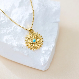 Gros plan du pendentif œil maléfique doré avec perle bleue sur fond de pierre blanche