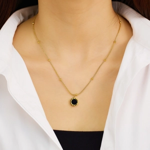 Detail view of a gold-plated heart necklace featuring Roman numerals on a black pendant
