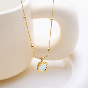 Detail of gold snake chain with small beads and Roman numeral shell pendant on a white tray