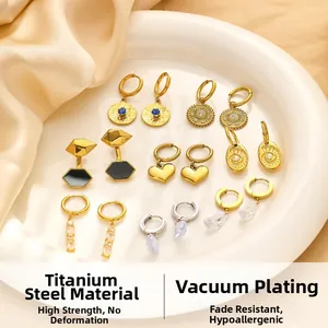 Flat lay of gold titanium steel earrings with heart and solar charms on a ceramic plate