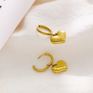 Detail of gold heart earrings on white fabric showing metallic mirror finish and texture
