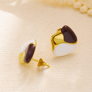 Detailed close-up of gold geometric earrings with white and brown enamel on beige texture