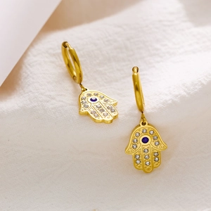 Macro detail of gold Hamsa Hand earrings with blue gemstone and white crystals