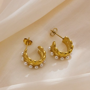 Détail de créoles dorées en forme de C avec perles sur tissu de satin blanc