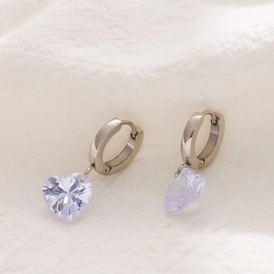 Macro shot of silver heart hoop earrings with light purple gemstone on white fabric