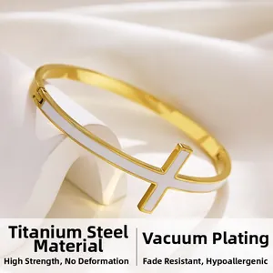 Dettaglio di un bracciale in acciaio titanio dorato con croce in smalto bianco decorativa
