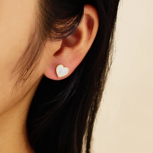 Close-up of heart-shaped gold stud earring with glitter inlay worn by model