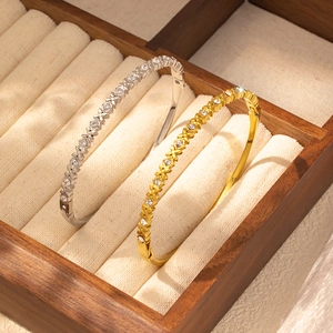 Dettaglio di braccialetti rigidi oro e argento con piccoli motivi floreali e cristalli
