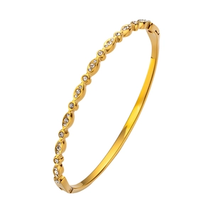 Detalle de brazalete de acero de titanio dorado con diseño ondulado y cristales