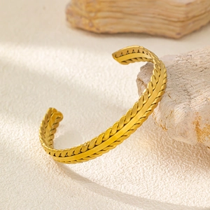 Dettaglio macro del bracciale rigido dorato a forma di C su superficie in pietra