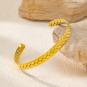 Dettaglio macro del bracciale dorato a C con trama a spiga su supporto di pietra