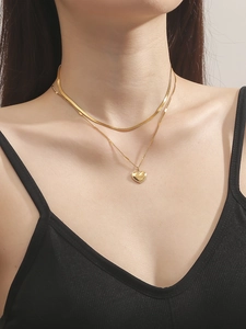Nahaufnahme einer zweilagigen Goldkette mit flacher Schlangenkette und Herzanhänger