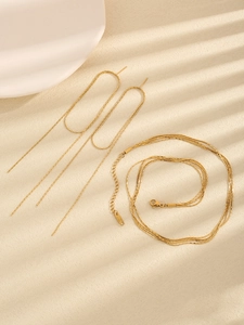 Macro view of gold multilayer necklace and long fringe earrings on ceramic display