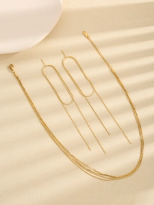 Close-up of minimalist gold layered necklace and geometric tassel earrings on beige surface