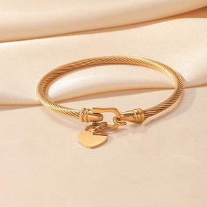 Golden twisted cable bangle with heart padlock charm and hook clasp on silk background