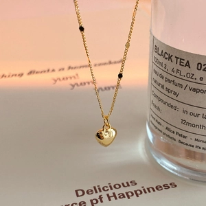 Detail of a golden heart pendant necklace featuring black beads in warm artistic lighting