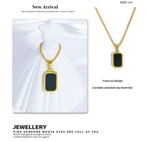 Détail du collier à chaîne carrée dorée avec pendentif rectangle noir sur fond blanc épuré
