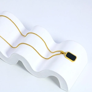 Collier chaîne box dorée avec pendentif rectangulaire noir sur support de présentation