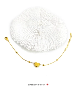 Detail of gold heart pendant bracelet with bead chain and lobster clasp on coral base