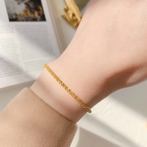 Detail shot of a sparkling gold titanium woven chain bracelet on a model's wrist