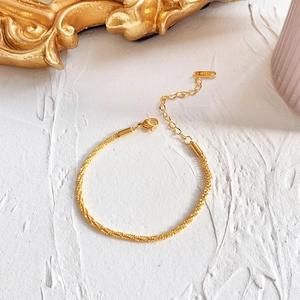 Detailed view of gold-plated woven twist bracelet with 18KGP tag and lobster clasp