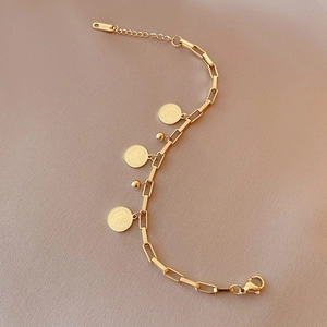Détail de breloques pièces dorées et maillons rectangulaires sur bracelet acier titane