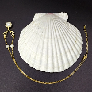 Elegante collana dorata con perle di zircone e motivo a corno su fondo di conchiglia bianca